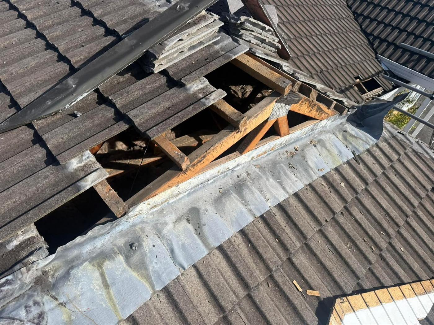 A stripped roof valley with the old valley iron exposed and tiles stacked to one side