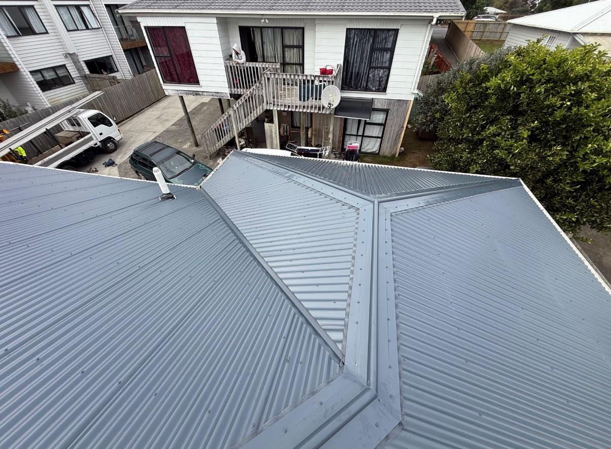 A completed light grey long-run re-roof seen from above the ridge