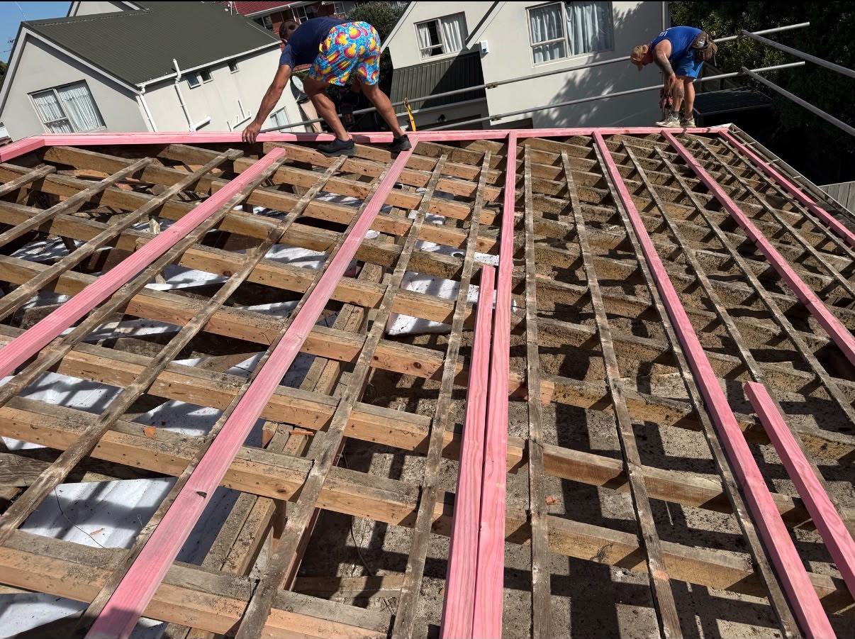 Two roofers setting out battens across a stripped roof